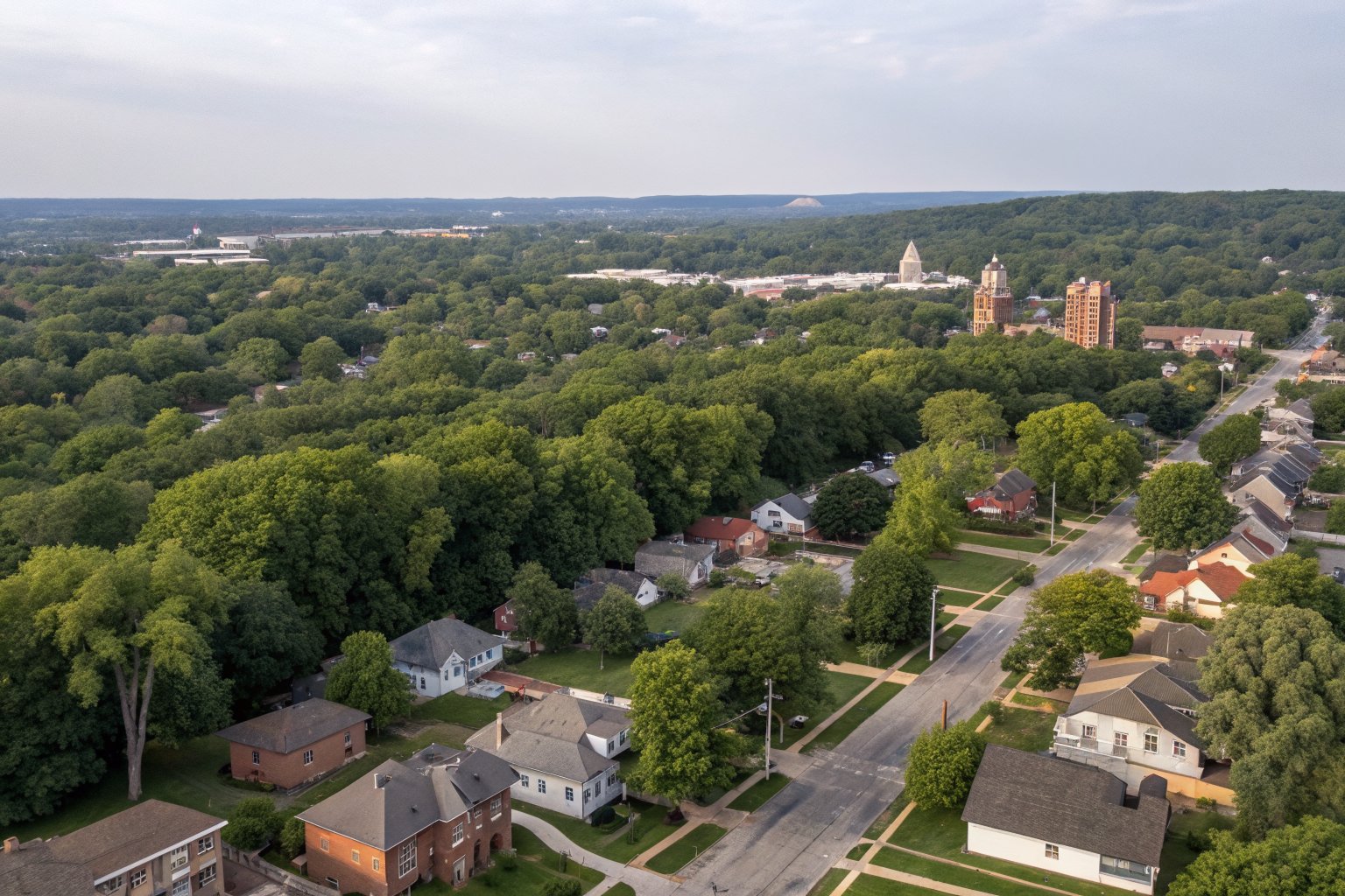 Aerial view of a leafy neighborhood of shingle-roofed houses with a small downtown in the distance
